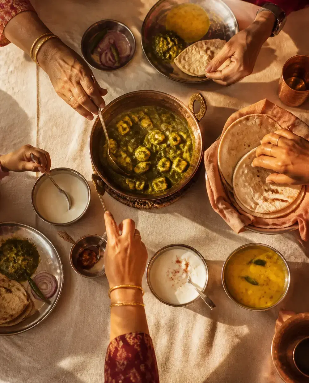 A family sharing palak paneer, rotis, dal and curd at one table